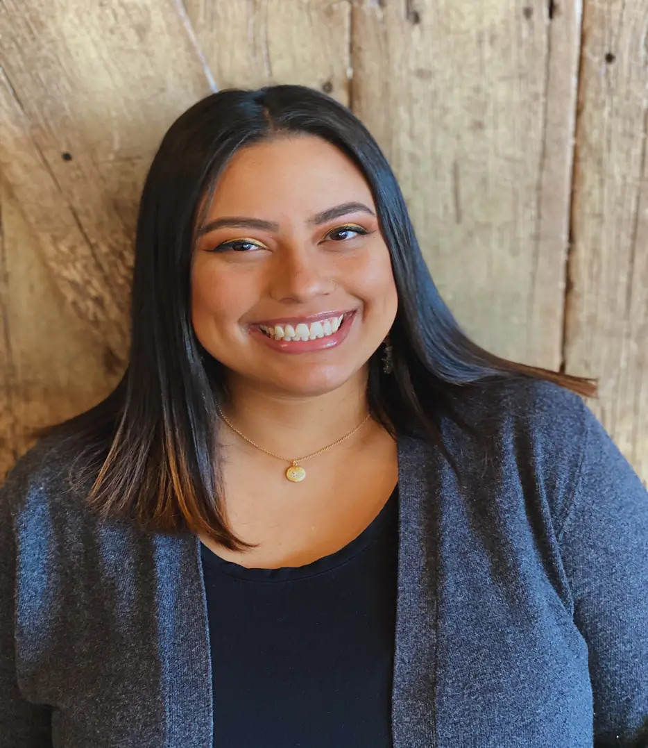 A smiling woman with straight brown hair against a wooden background.