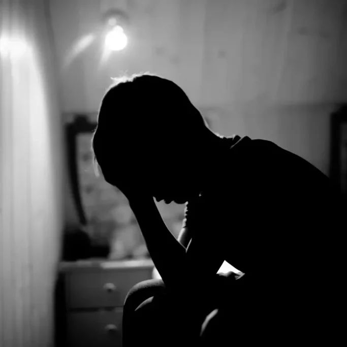 Silhouette of person sitting in dimly lit room.